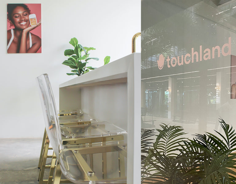 Inside of touchland office building, chair with tableand plant, peach writing on window that says "Touchland"