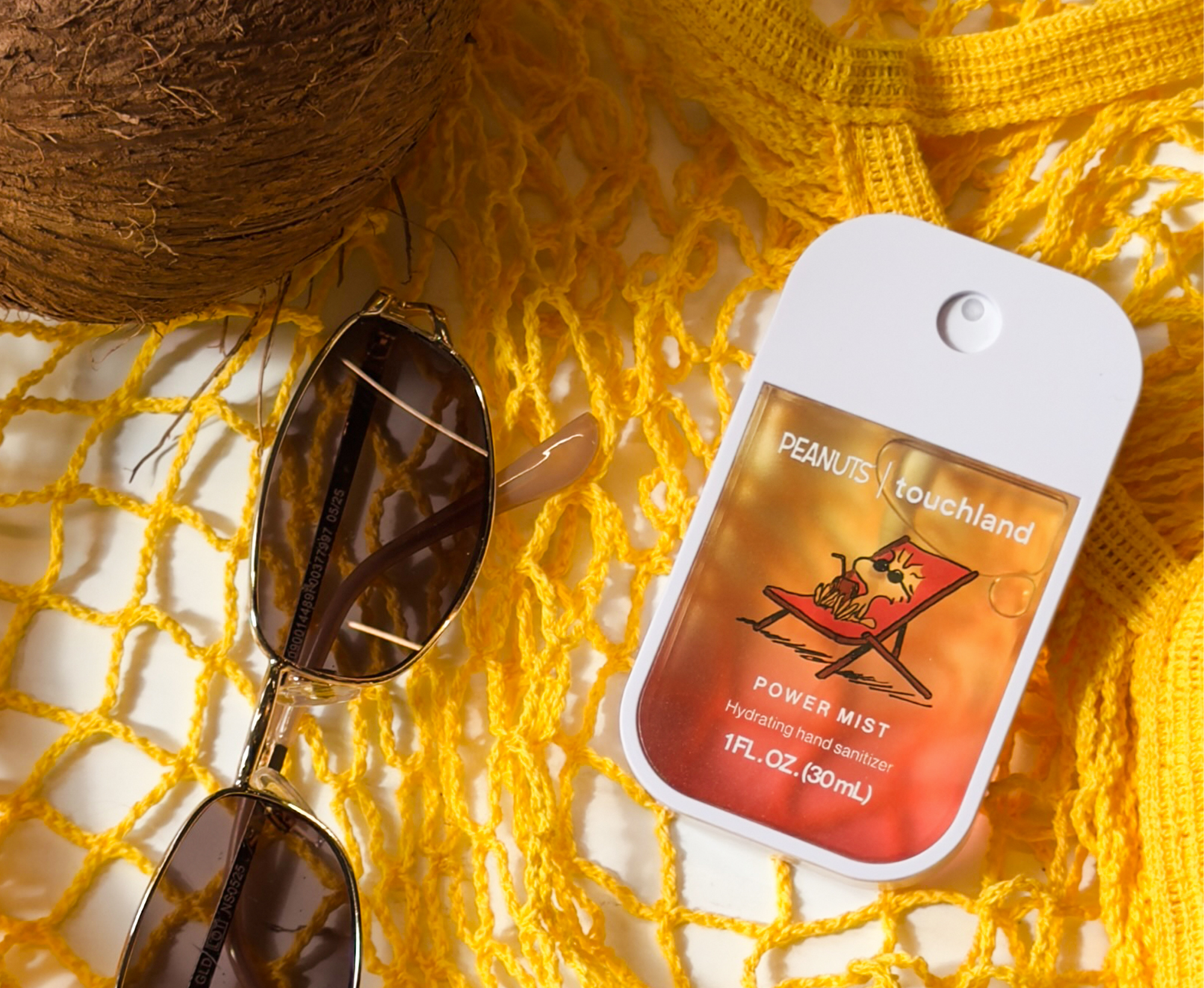 Peanuts touchland power mist on a yellow textured surface with sunglasses and a coconut.