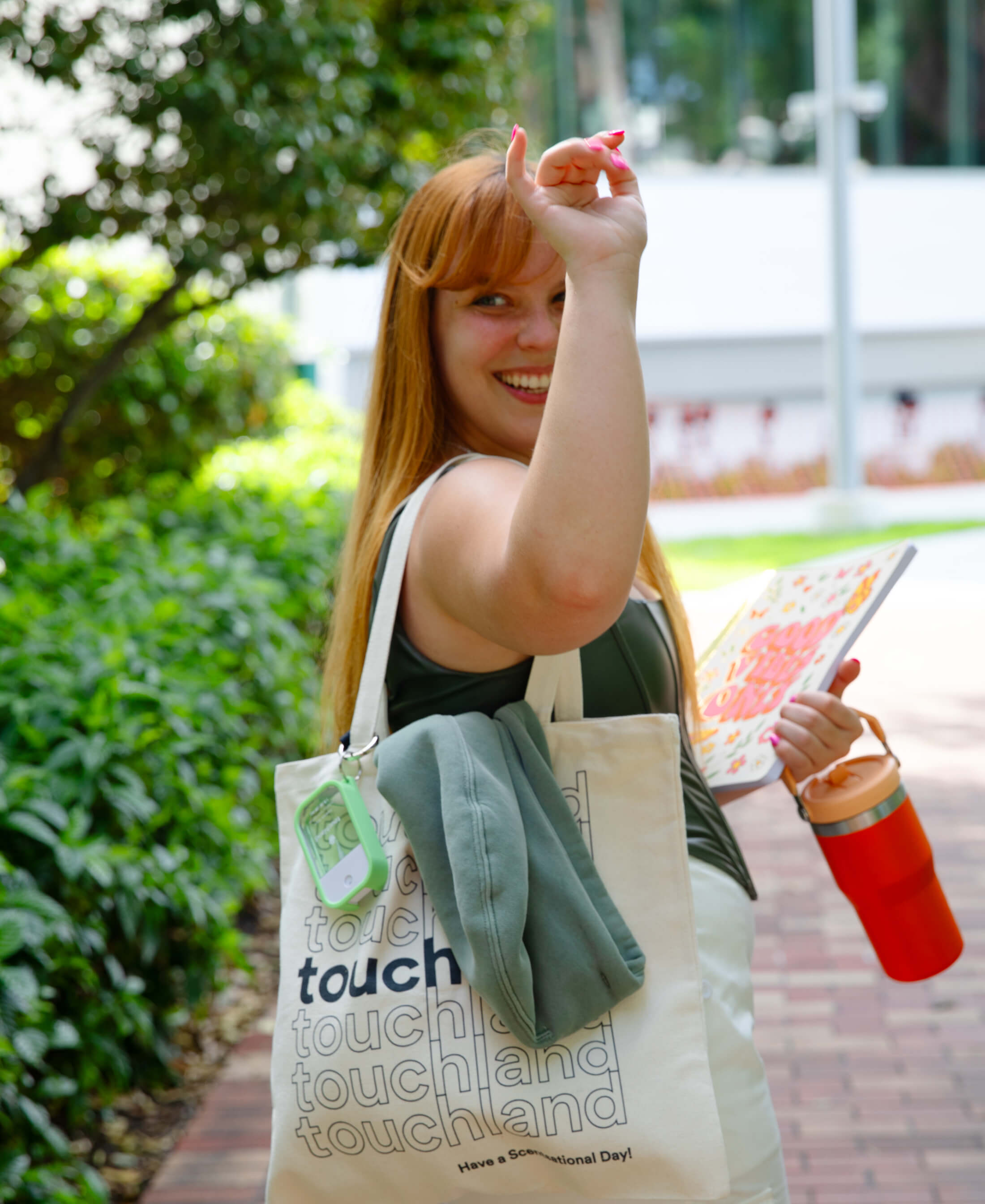 Female model waving goodbye with an Applelicious Power Mist attached to a customized Touchland tote bag.