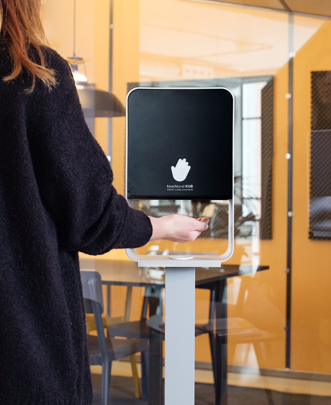 Woman wearing black cardigan facing away from the camera using jet black kub dispenser on stand in office setting