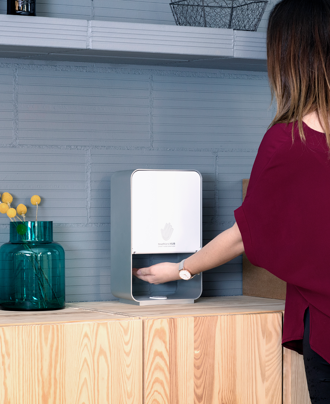 Woman in red shrt with back to camera using red kub dispenser on table next to vase