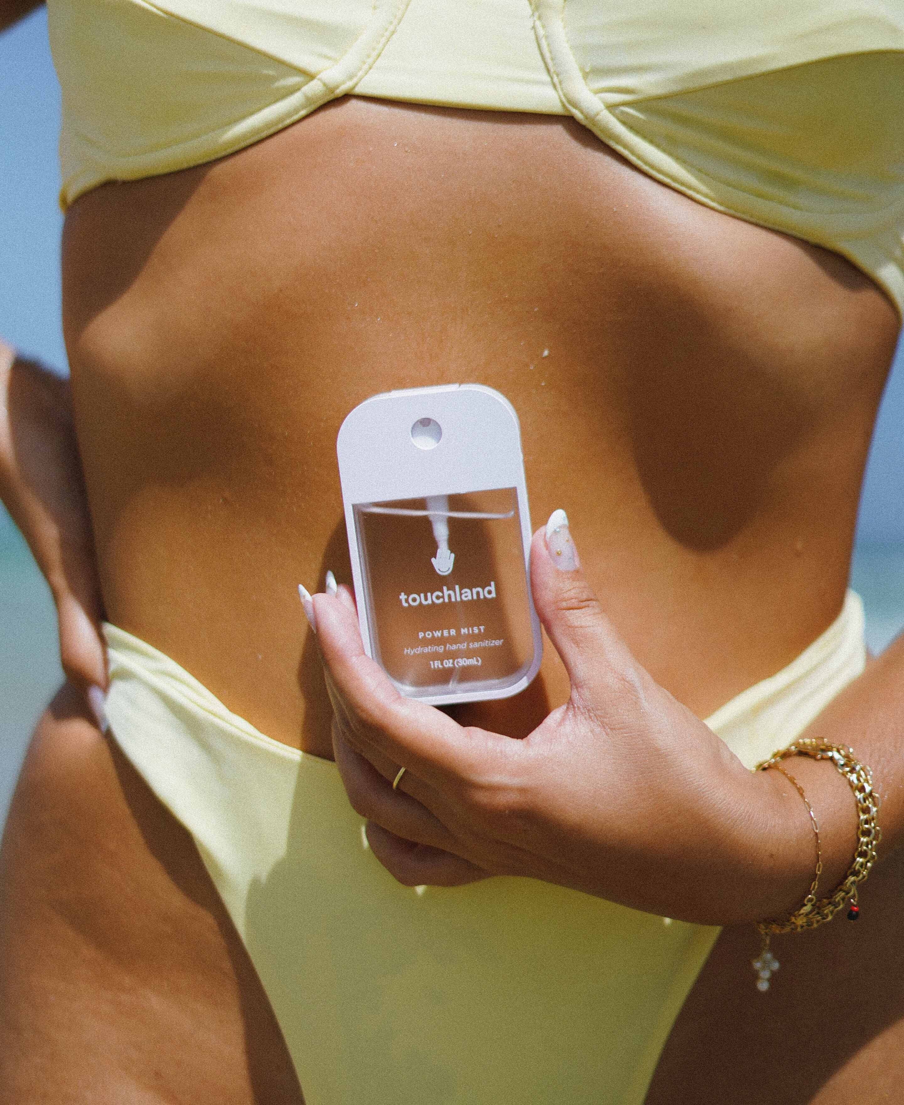 Woman with yellow bikini at the beach holding a Power Mist hand sanitizer