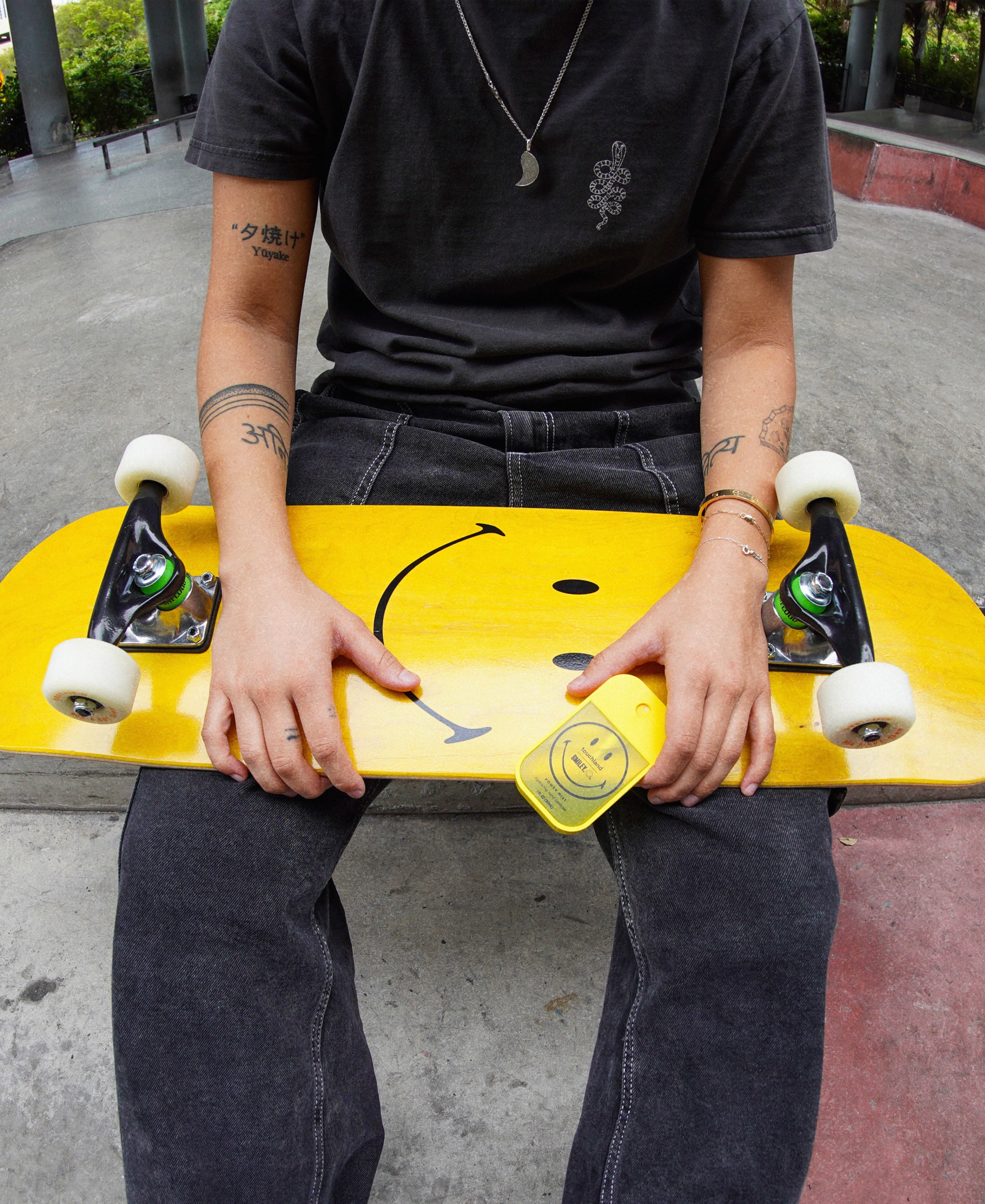 Female model sitting with a Smiley yellow skateboard on her legs while holding a smiley Mango Passion Power Mist