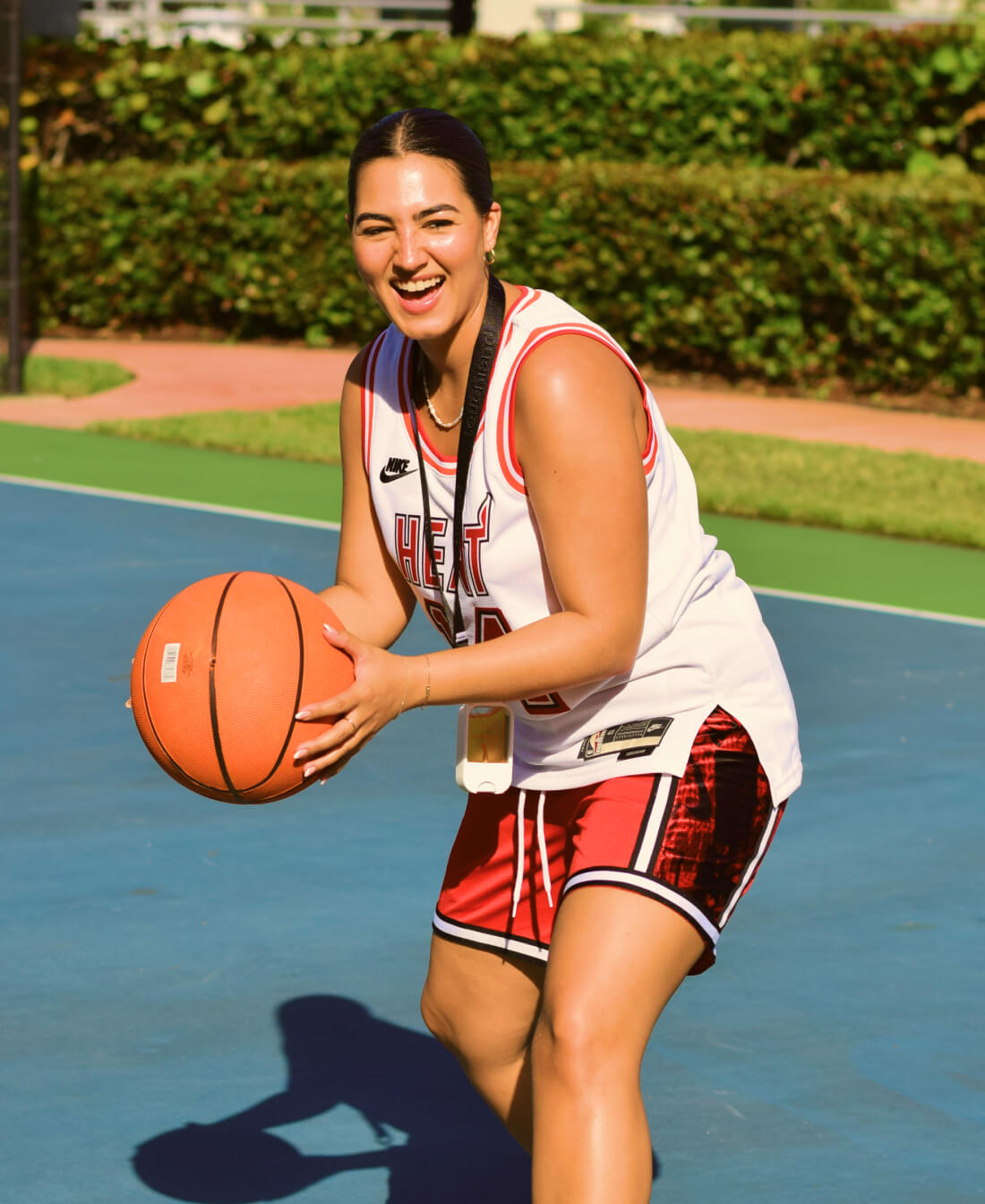 A woman smiling while playing basketball with the Citrus Grove Power Mist attached to a black Touchland Lanyard around her neck.