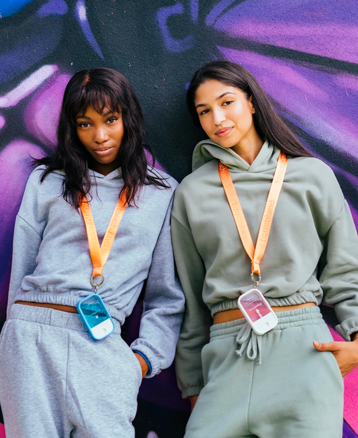 Two girls in matching sweat sets wearing power mist lanyards and looking at the camera